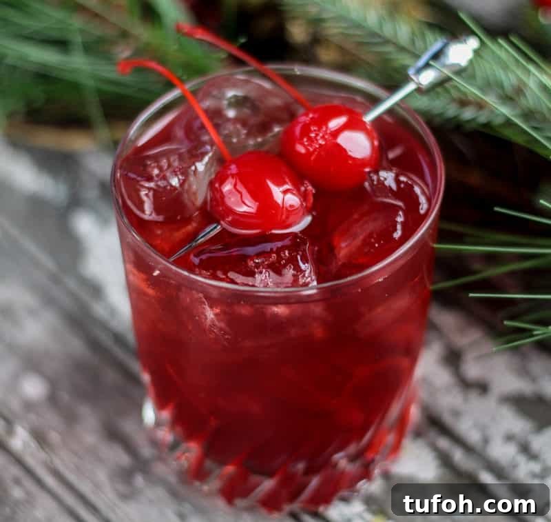 25+ Romantic Valentine's Day Cocktails and Toasting Drinks 11 red cherry cocktail with two maraschino cherries for garnish next to greenery