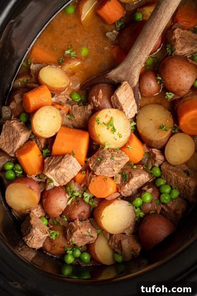 Slow-Cooker Beef Stew with Tender Chunks and Veggies 3 Close up of vegetables and stew meat in the crockpot with a wooden spoon scooping the beef stew.