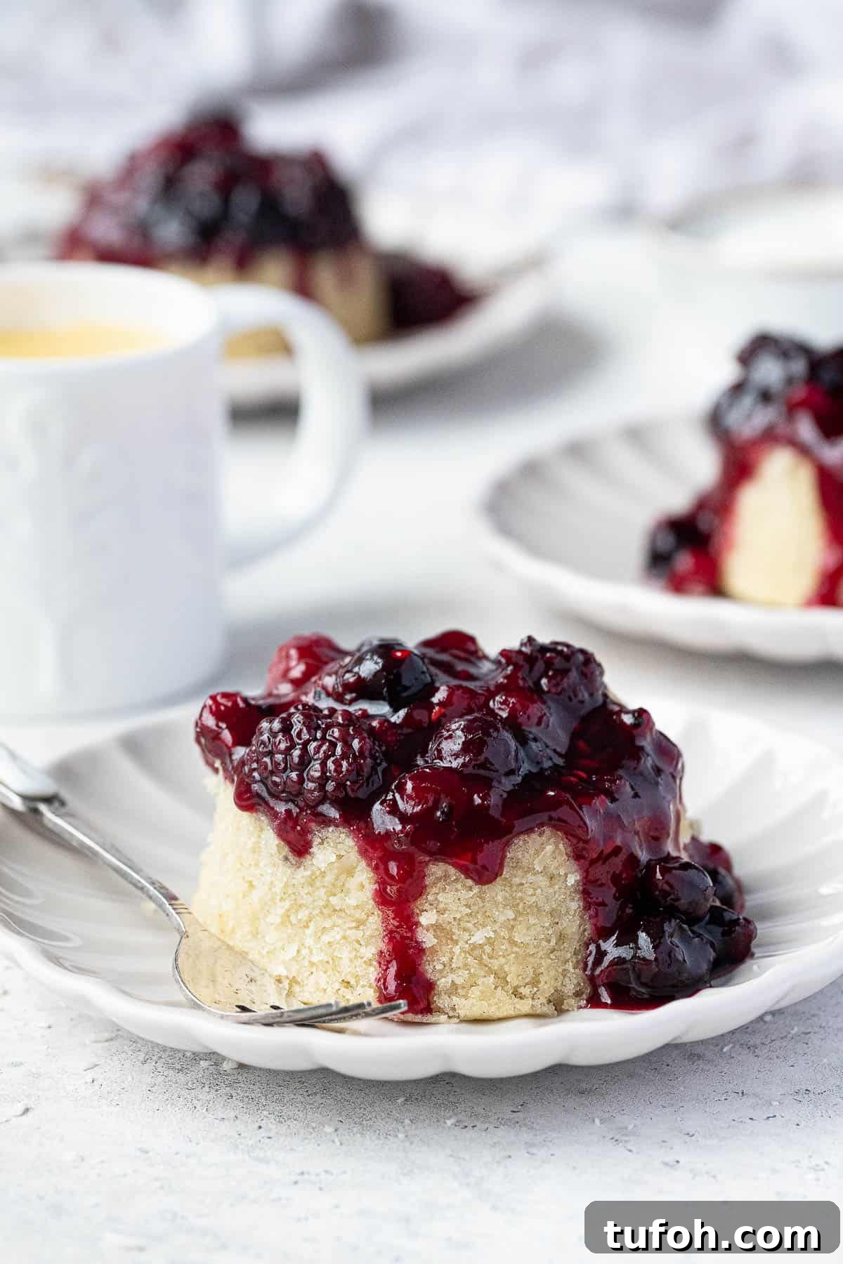 Vegan Berry & Coconut Steamed Puddings Recipe 2 Three steamed berry and coconut puddings on plates with a jug of custard.