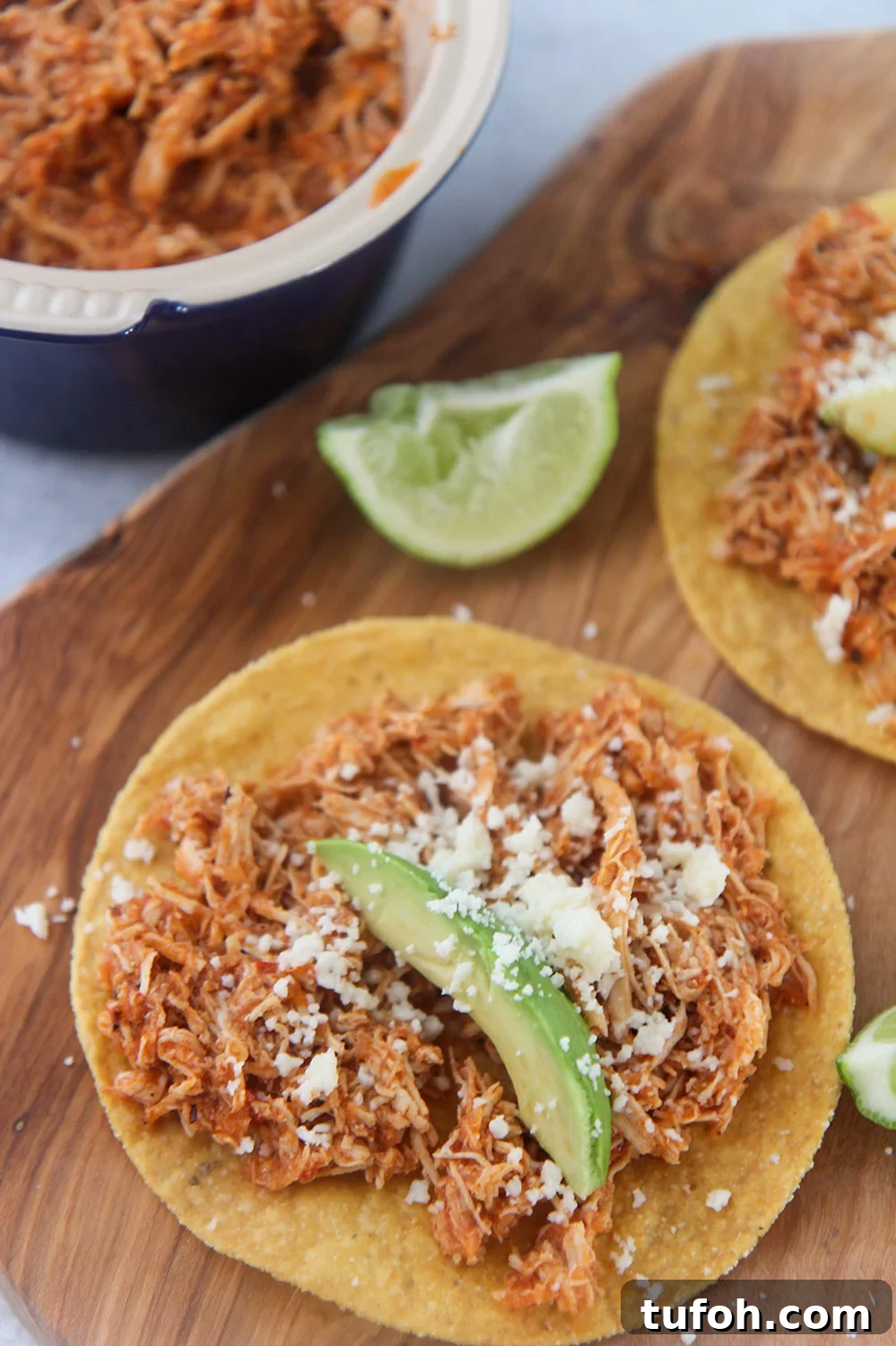 chicken tinga tostadas on a wooden board with lime wedges on the side.