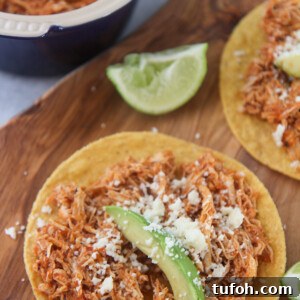 chicken tinga tostadas on a wooden board with lime wedges on the side.