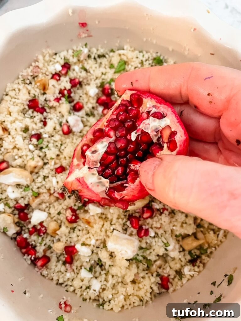 Pomegranate Mint Couscous Salad with Citrus Dressing 3 A pomegranate being held over the couscous dish