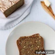 Sourdough Danish Rugbrød Rye Loaf Recipe 10 Rye bread slices on a plate next to a loaf of rye bread and a wooden knife with butter