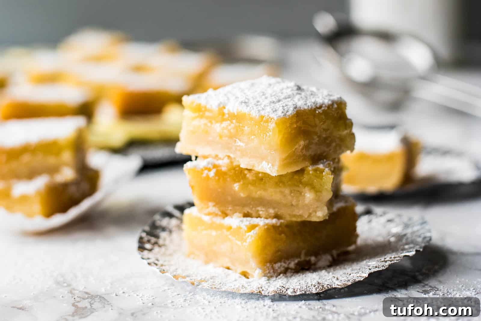 21 Kid-Friendly Treats to Make Together (Simple Recipes) 3 A stack of three lemon bars on a plate with more lemon bars in the background.