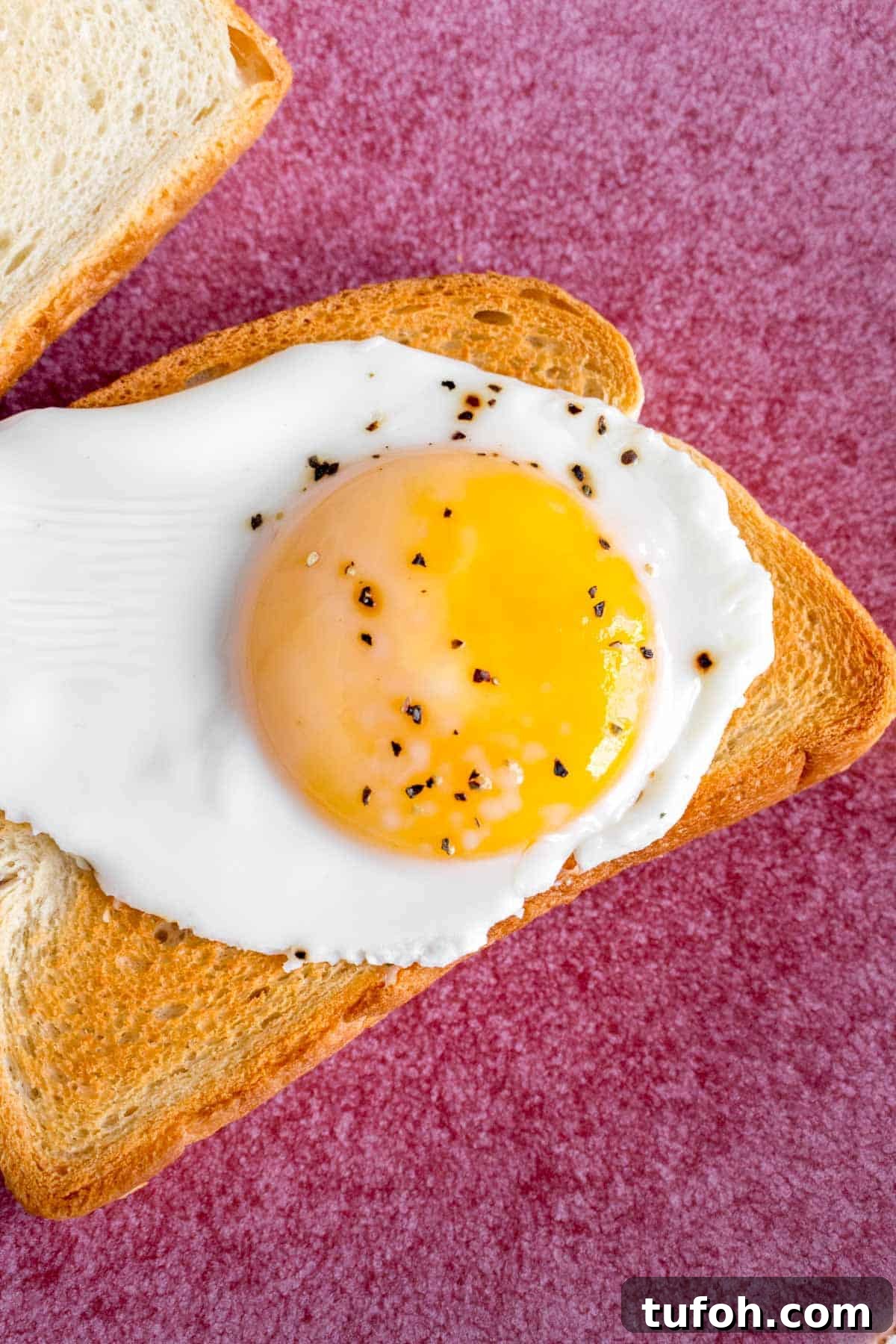 Close up of a sunny side up egg on a piece of toast.