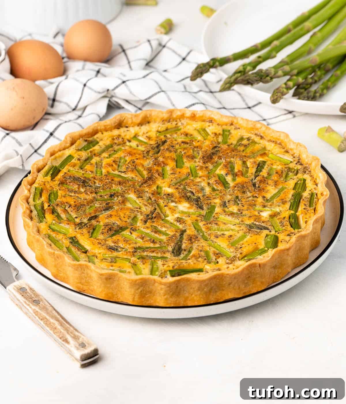 Feta and Asparagus Quiche Recipe for Spring Brunch 7 Side view on the quiche placed in a large white plate with ingredients in the background.