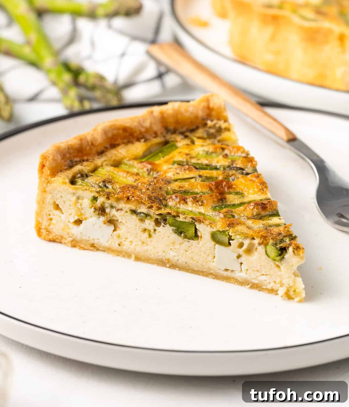 Feta and Asparagus Quiche Recipe for Spring Brunch 9 One slice on a small white plate with a fork in the background.