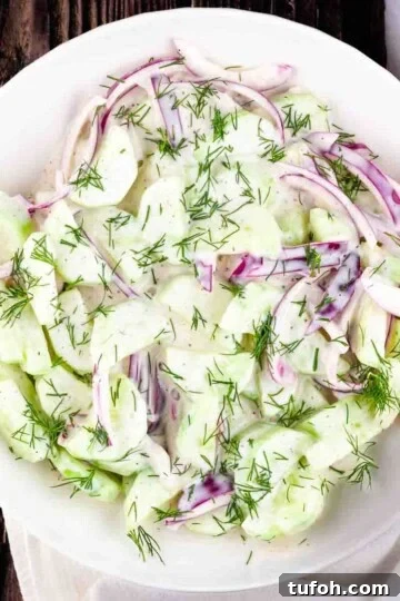 Creamy cucumber and onion salad in a white serving bowl.
