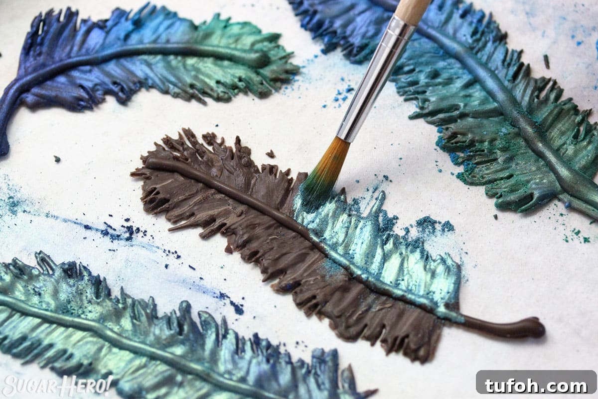 Decadent Chocolate Feather Cookies Recipe 5 Brushing teal luster dust on a chocolate feather, with blue and green chocolate feathers scattered around.