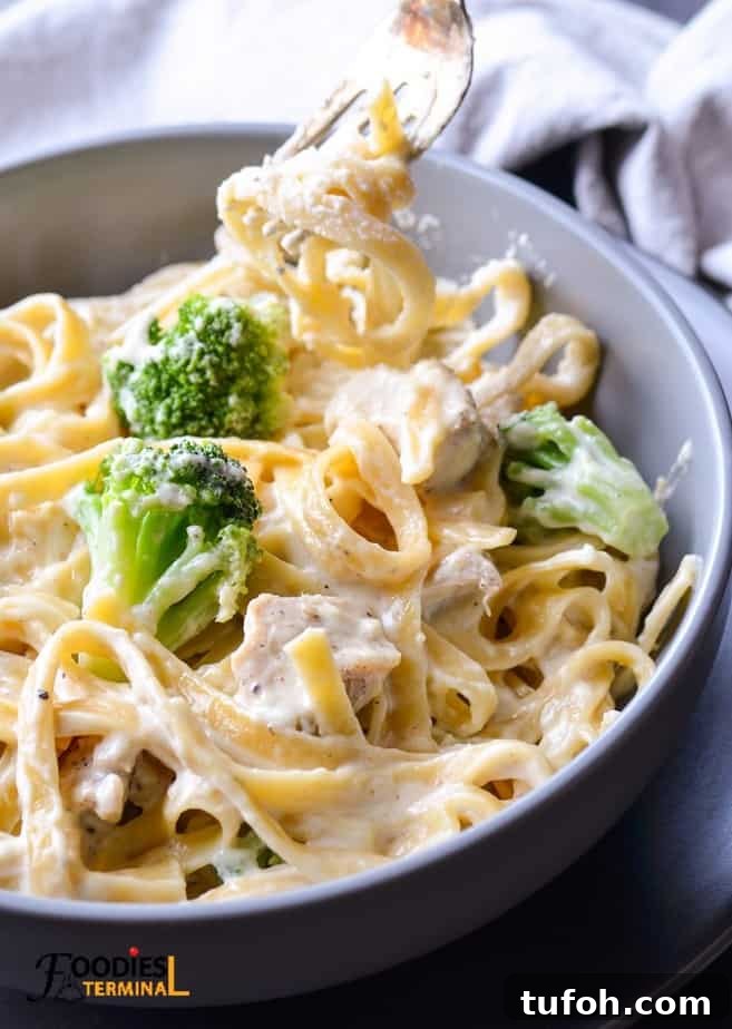 Creamy Instant Pot Chicken Fettuccine Alfredo with Broccoli 4 creamy chicken fettuccine alfredo with broccoli being lifted with a fork from a grey bowl