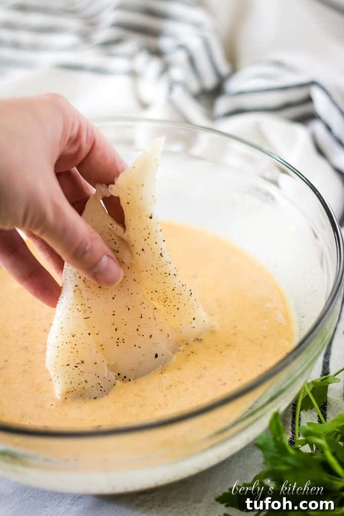 Crispy Beer-Battered Cod Recipe for Perfect Fish Fry 5 A piece of cod being dipped into the beer batter.