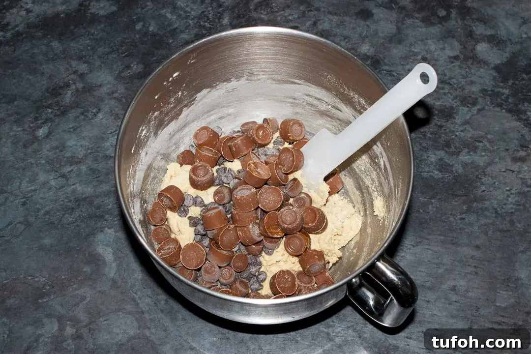 Cookie dough, Rolos and chocolate chips in the bowl of an electric stand mixer with a spatula