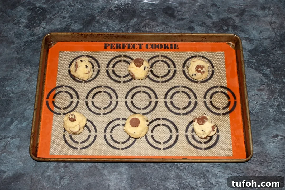 6 Rolo cookie dough balls spaced out on a large lined baking tray