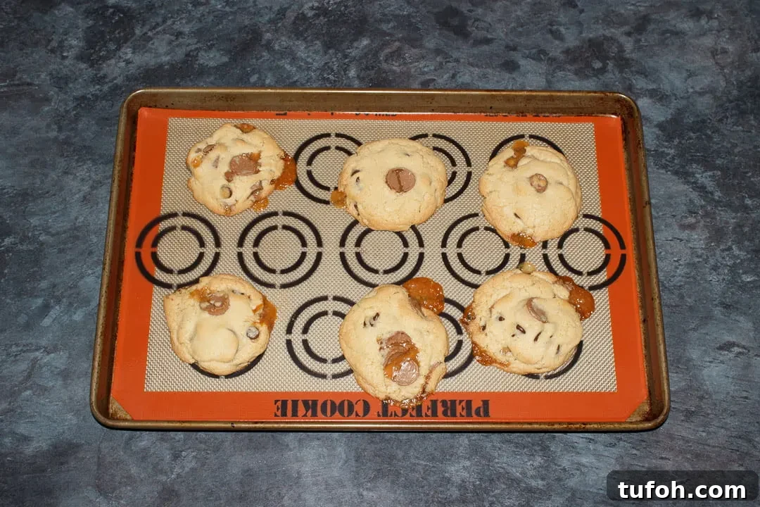 6 baked Rolo cookies spaced out on a large lined baking tray with caramel oozing out