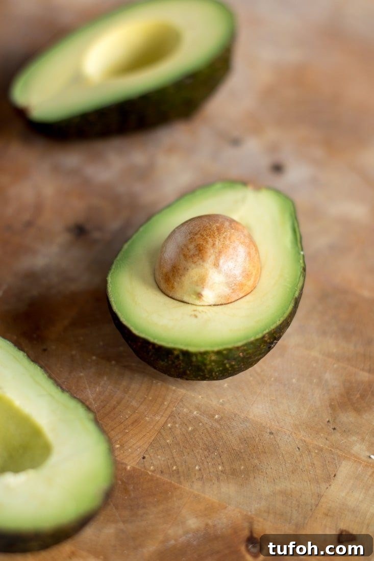 Creamy Vegan Guacamole Recipe for Parties and Snacks 3 Avocado halves on a wooden board.