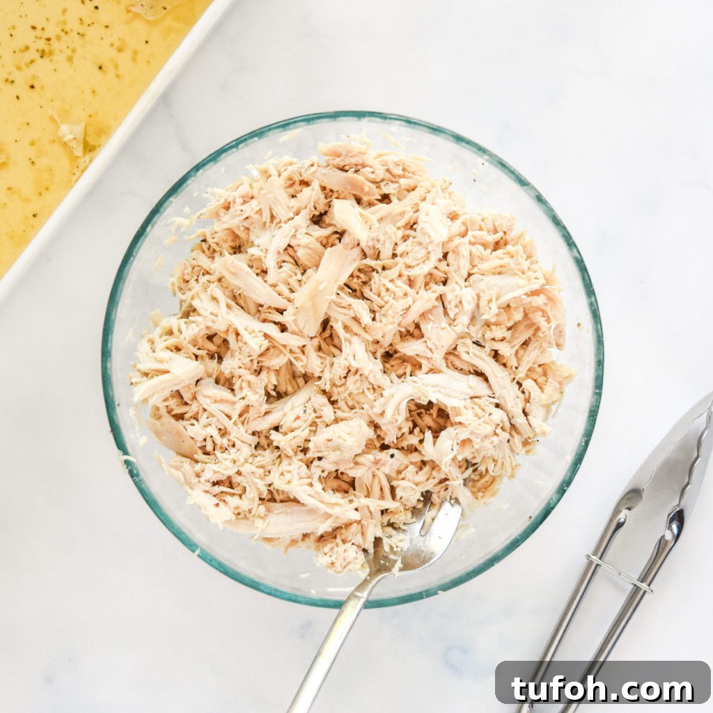 shredded chicken breasts in a glass bowl with large fork.