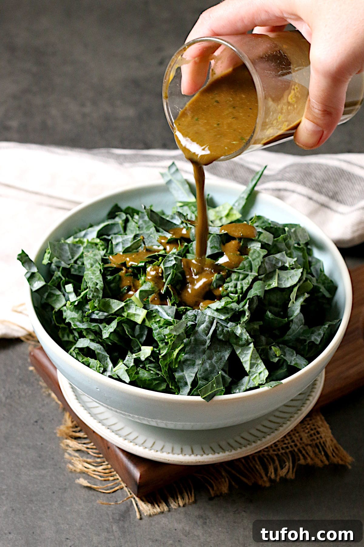 A hand pouring Basil Balsamic Vinaigrette onto a bowl of shredded kale.