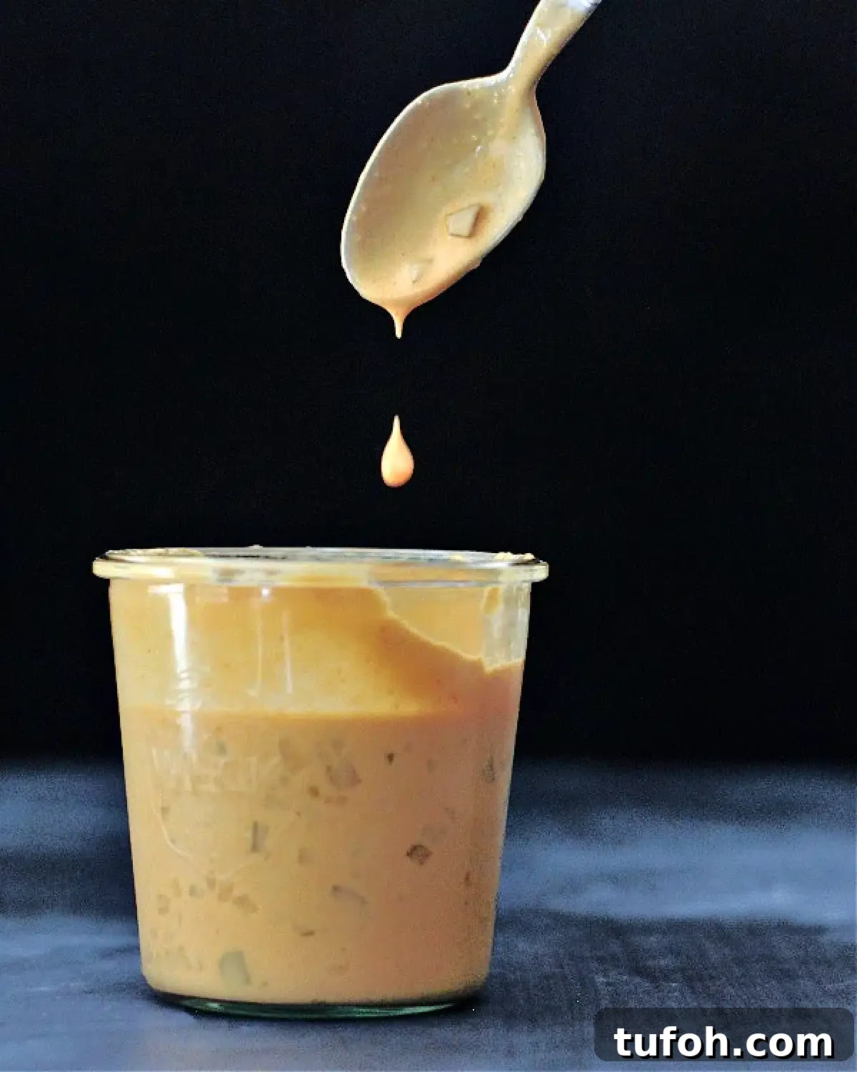 Vegan Thousand Island Dressing @spabettie #dairyfree #glutenfree #vegan #frysauce A large glass Weck jar of vegan thousand island dressing, with a spoon dripping sauce above the jar against a black background.