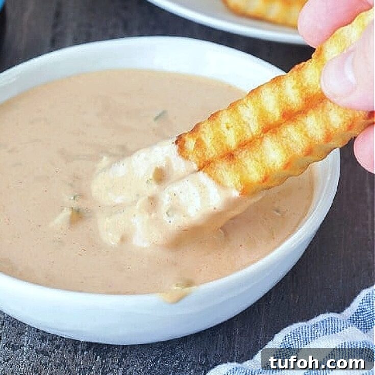 Close up of krinkle cut French fries being dipped into a bowl of Thousand Island dressing.