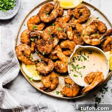 Grilled Blackened Shrimp with Zesty Cajun Seasoning 2 grilled blackened shrimp on a plate with fresh lemon and dipping sauce