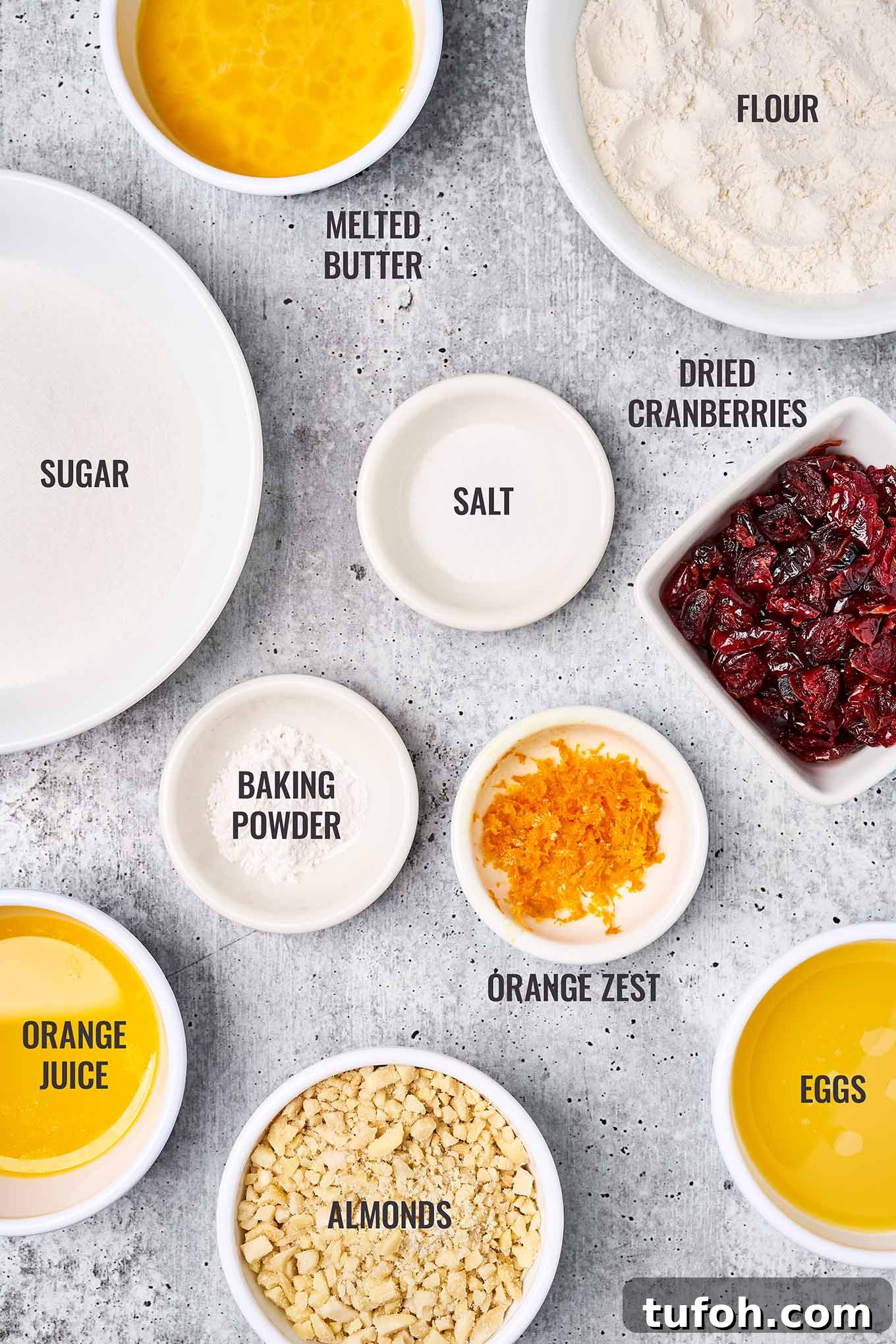 Cranberry Orange Bar Recipe — Tart, Chewy Holiday Dessert 3 A labeled, overhead view of the ingredients for cranberry orange bars including baking ingredients, orange zest, dried cranberries, orange juice, and almonds.