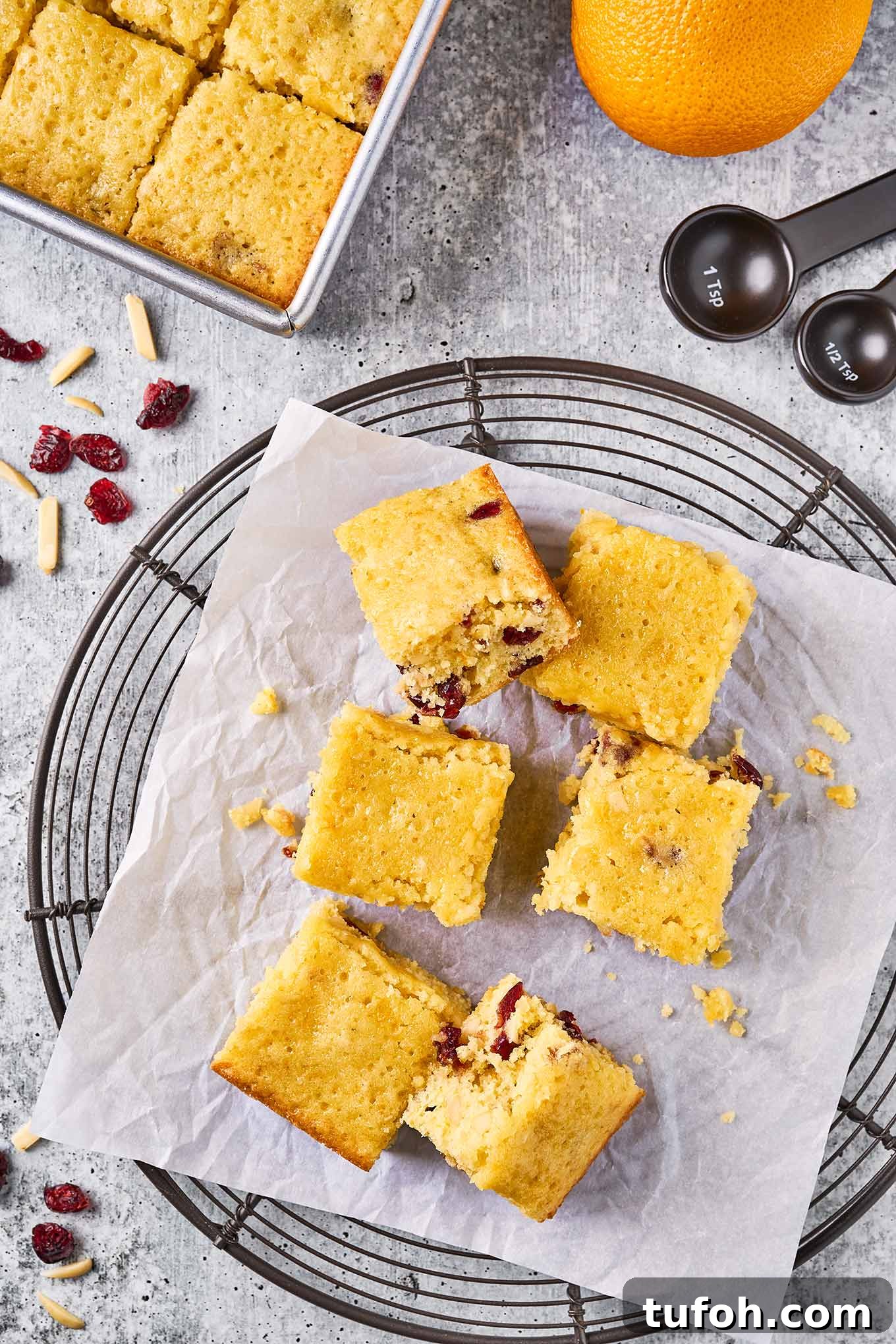 Cranberry Orange Bar Recipe — Tart, Chewy Holiday Dessert 6 An overhead view of a round cooling rack with cranberry orange bars on a piece of parchment paper, surrounded by the baking pan and other ingredients.