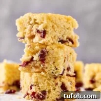 Cranberry Orange Bar Recipe — Tart, Chewy Holiday Dessert 8 Three cranberry bars stacked on a cooling rack, showing their dried cranberries, almonds, and orange zest.