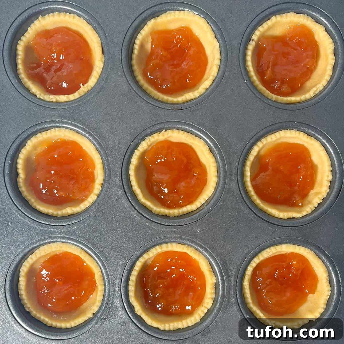 Hertzoggies: South African Jam and Coconut Tartlets Recipe 10 Filling the pastry cases with apricot jam for the jam and coconut tartlets.