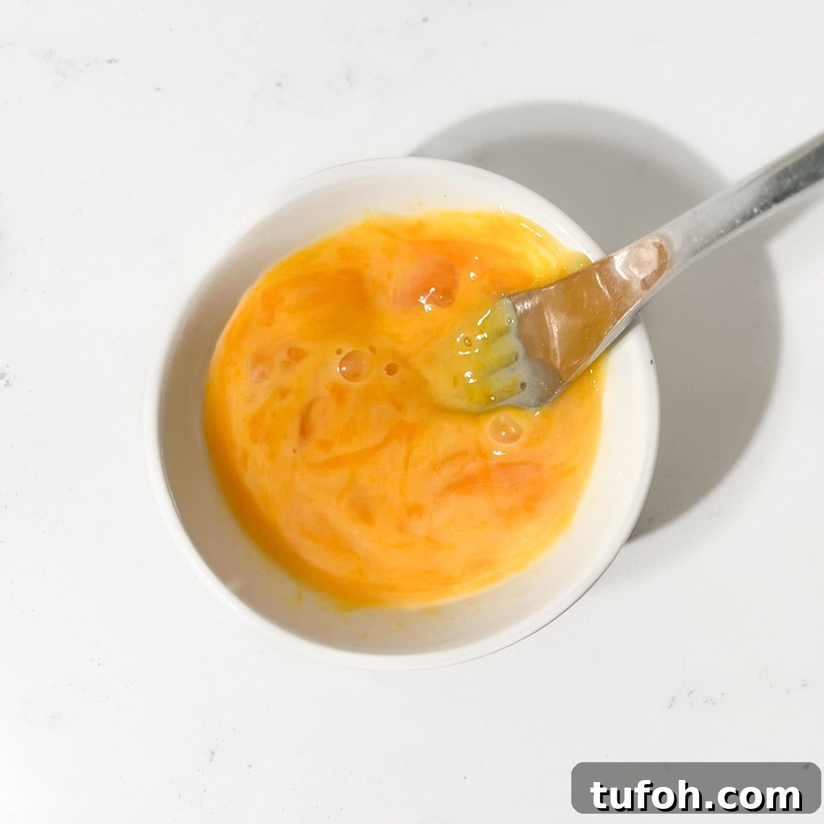 Hertzoggies: South African Jam and Coconut Tartlets Recipe 7 Mixing the egg yolks with cold water in a small white bowl.