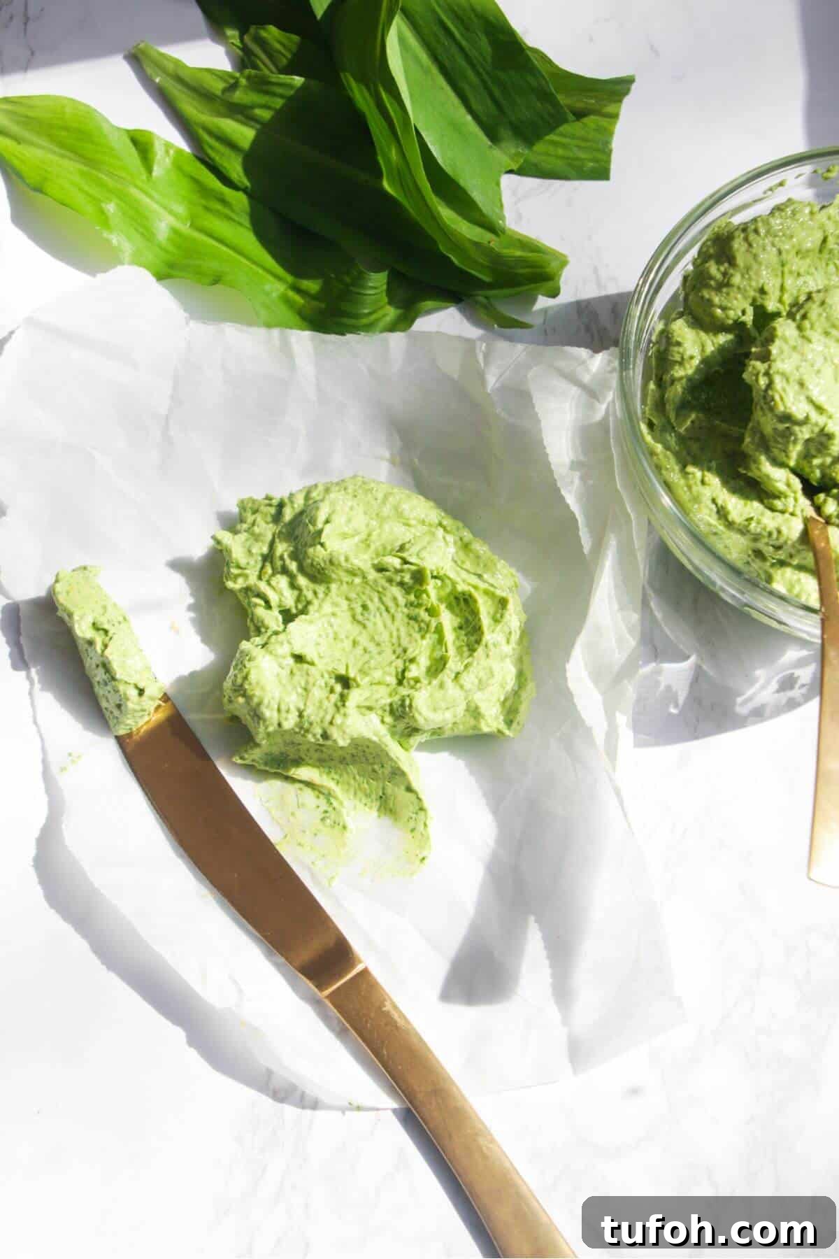 Wild garlic butter on a piece of baking paper with more wild garlic butter in a small glass bowl, with a god knife on the side.