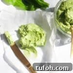 Wild garlic butter on a piece of baking paper with more wild garlic butter in a small glass bowl, with a gold knife on the side.