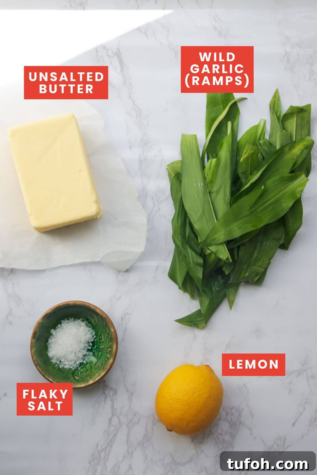 Ingredients for wild garlic butter laid out on a white marble background and labelled.