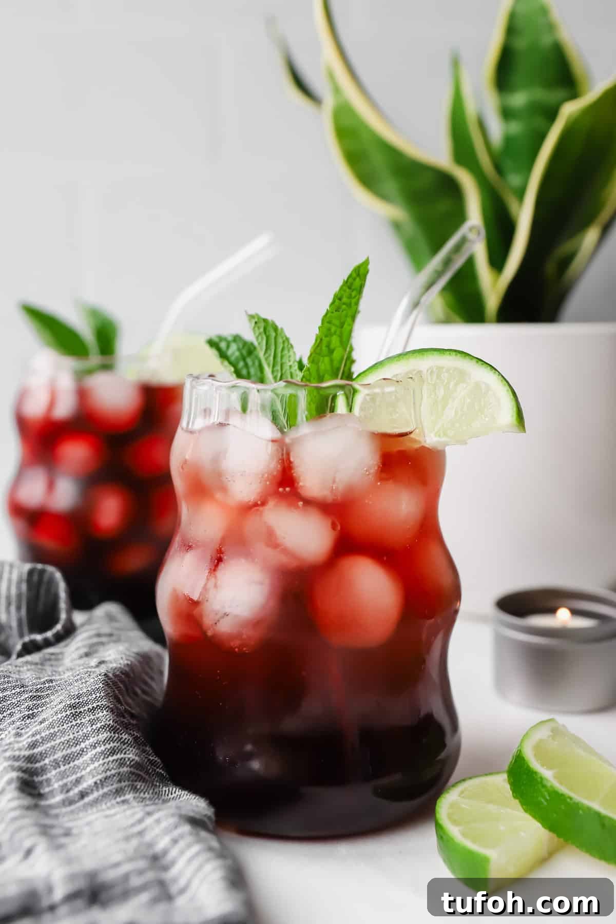 Relaxing Sleepy Girl Mocktail Recipe — Caffeine-Free Nightcap 2 Two glasses of iced tea garnished with lime wedges and mint leaves. A potted plant and sliced limes are in the background.