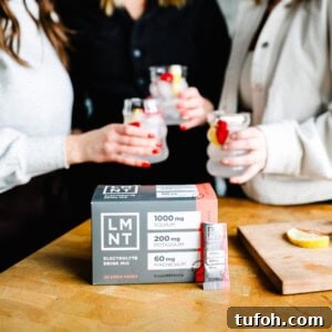 Relaxing Sleepy Girl Mocktail Recipe — Caffeine-Free Nightcap 4 Three friends enjoying drinks, including a refreshing sleepy girl mocktail, sit beside a box of LMNT electrolyte drink mix on the wooden table.
