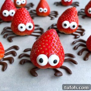 Strawberries decorated with candy eyes and chocolate legs to resemble cute spiders make fun, healthy bites—perfect for creative food recipes and party dishes, arranged on a light surface.