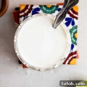 How to Make Mexican Crema at Home — Smooth, Tangy Recipe 11 Overhead of a glass filled with mexican cream sauce with a spoon dipping in.