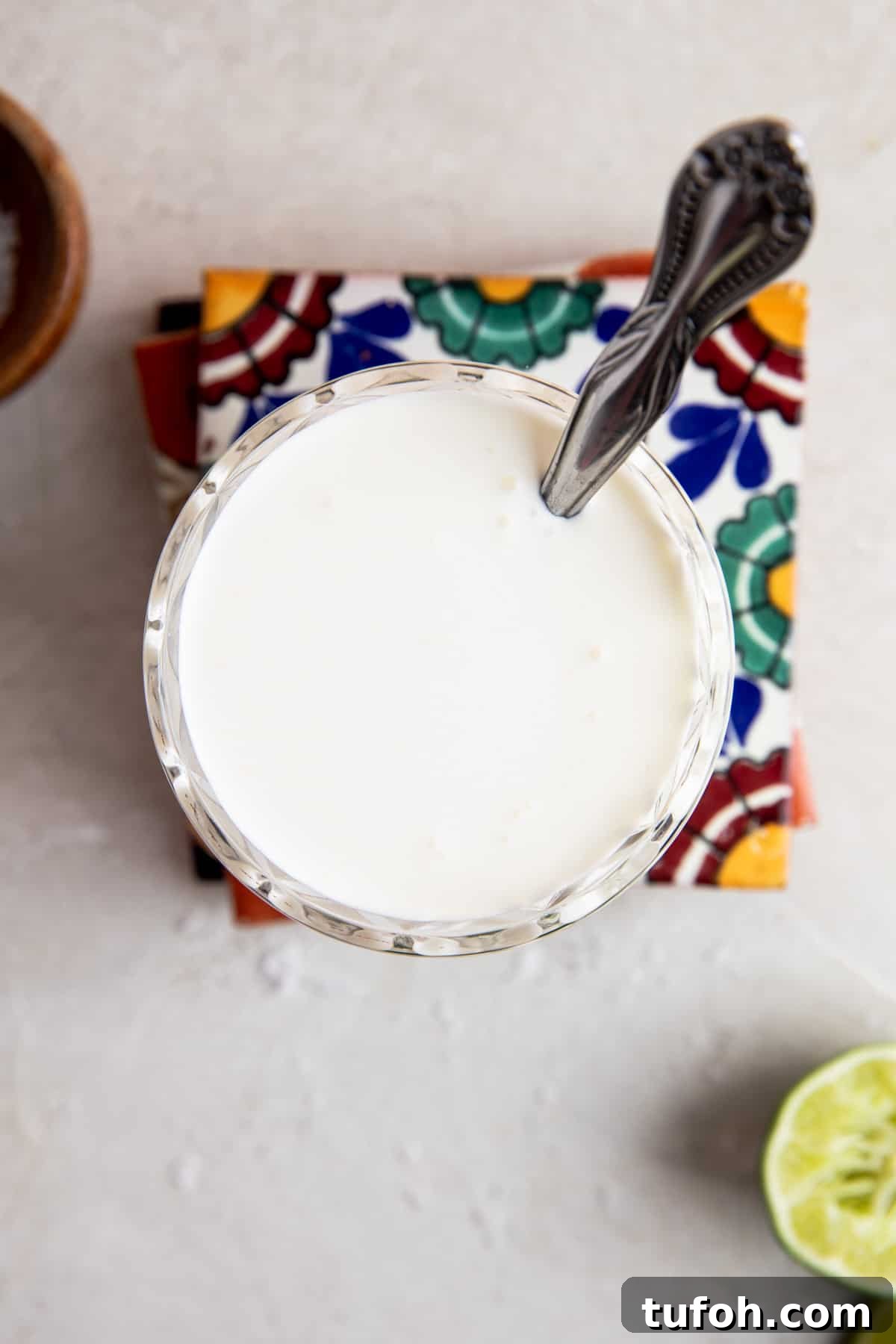 How to Make Mexican Crema at Home — Smooth, Tangy Recipe 5 Overhead of a glass filled with mexican cream sauce with a spoon dipping in.