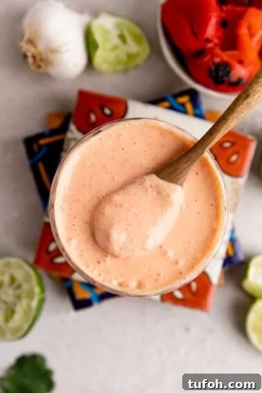 How to Make Mexican Crema at Home — Smooth, Tangy Recipe 6 Glass filled with red pepper crema with a wooden spoon scooping it up.