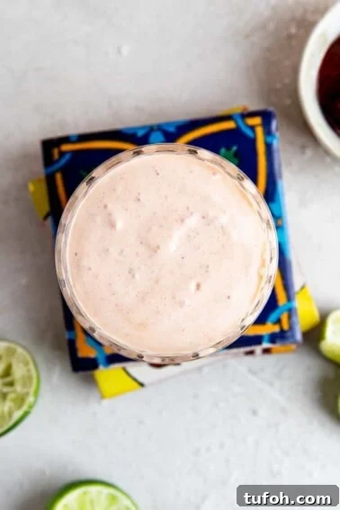 How to Make Mexican Crema at Home — Smooth, Tangy Recipe 7 Cup filled with chipotle crema on top of a stack of mexican tiles, lime wedges around it.