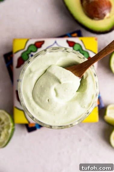 How to Make Mexican Crema at Home — Smooth, Tangy Recipe 8 Overhead view of a cup filled with light green colored avocado crema being scooped up with a wooden spoon.