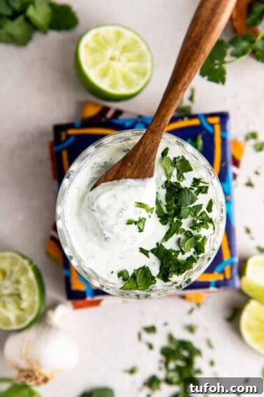 How to Make Mexican Crema at Home — Smooth, Tangy Recipe 9 Glass filled with cilantro lime crema topped with fresh diced cilantro and a wooden spoon to serve.
