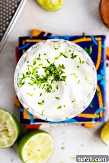 How to Make Mexican Crema at Home — Smooth, Tangy Recipe 10 Glass filled with smooth Lime Crema topped with lime zest. Sitting on top of mexican tiles.
