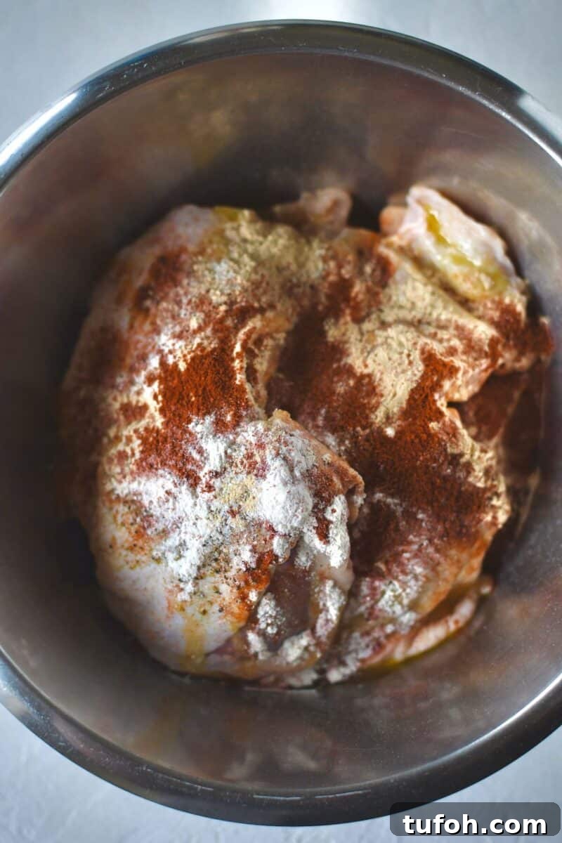 Juicy Grilled Chicken Thighs with Crispy Skin and Smoky Flavor 4 Chicken thighs in a bowl with the seasonings tossed over them.
