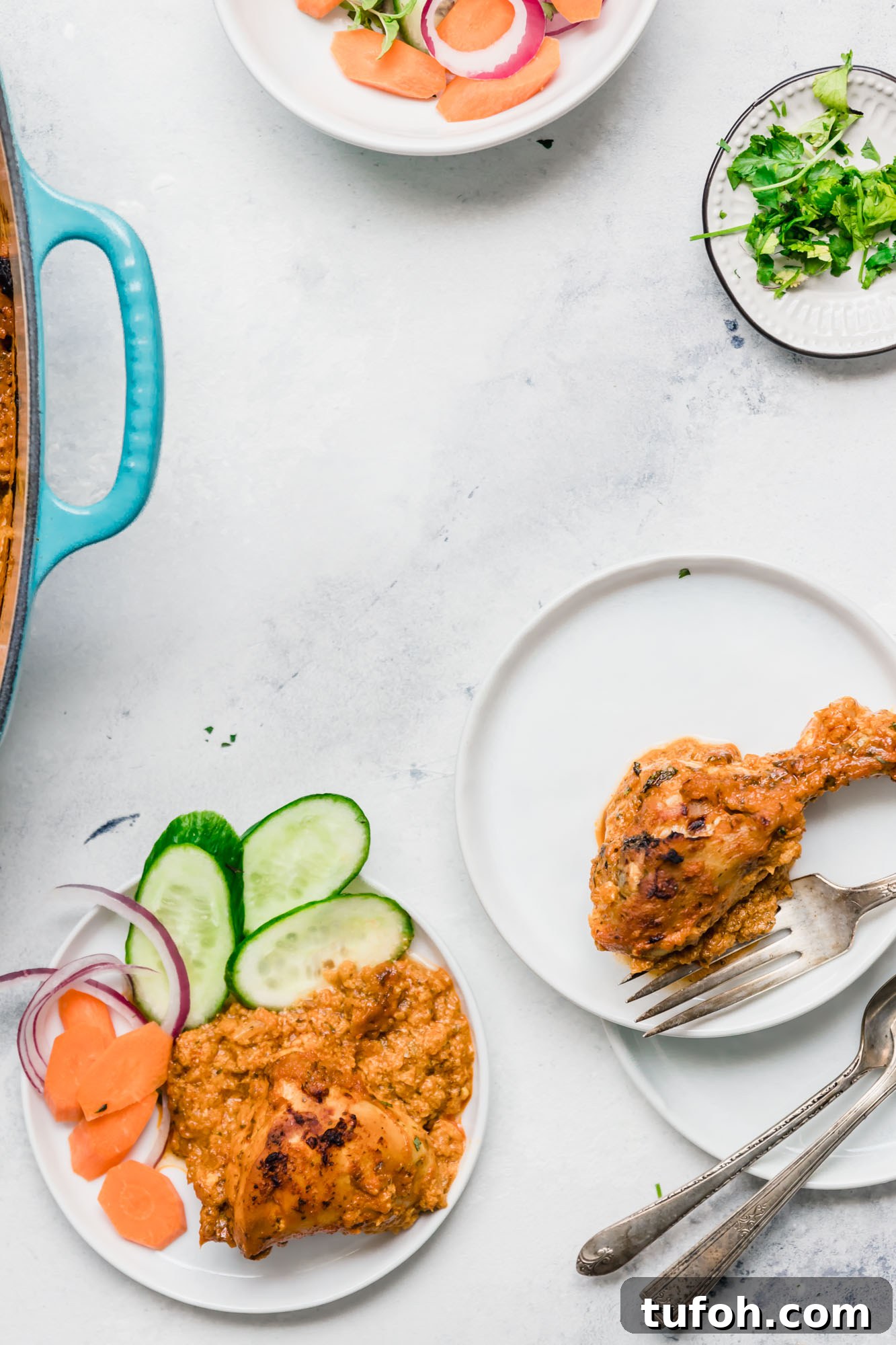 Oven-Baked Tandoori Chicken Curry Recipe 5 A round white plate of Baked Tandoori Chicken Curry alongside sliced cucumbers, carrots and red onion.