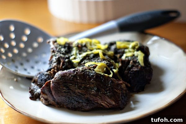 Finished ranchers roast beef topped with pepperoncini and gravy. Cooked ranchers roast beef on plate with pepperoncini on top