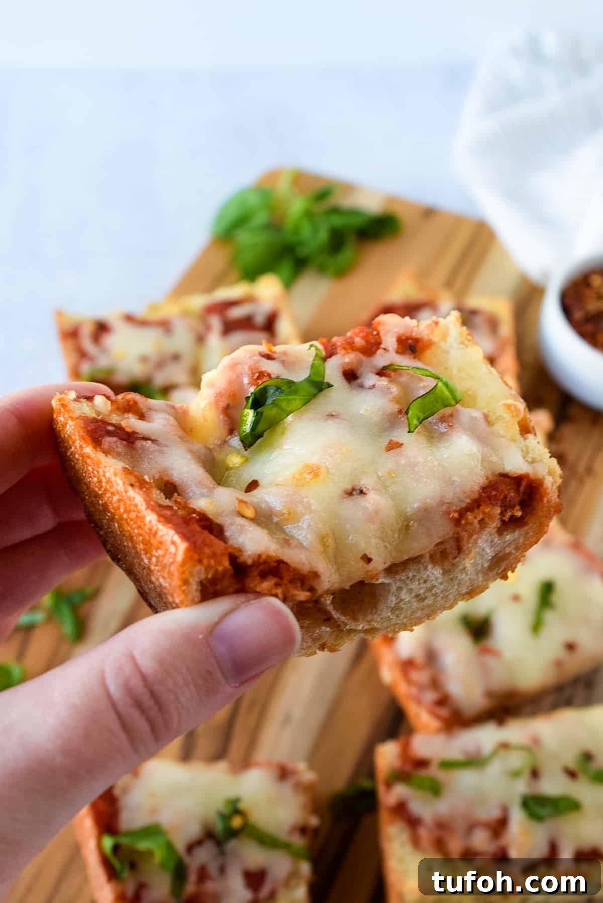 Crispy French Bread Pizza Made in the Air Fryer 4 A hand holding a slice of Air Fryer French Bread Pizza.