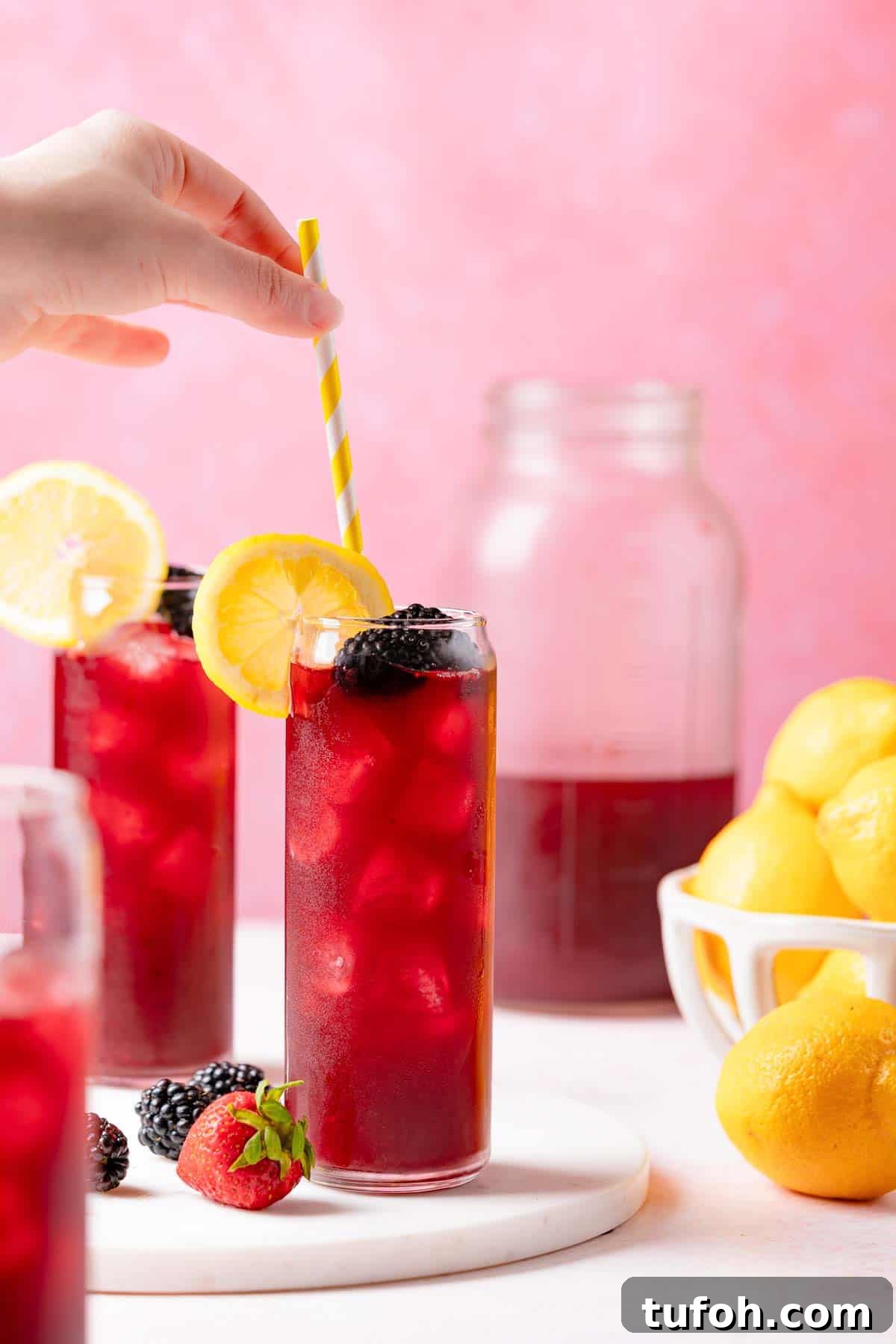 straw being placed in glass of berry lemonade next to two other glasses of lemonade.