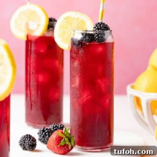 two glasses of berry lemonade garnished with lemon and blackberries.