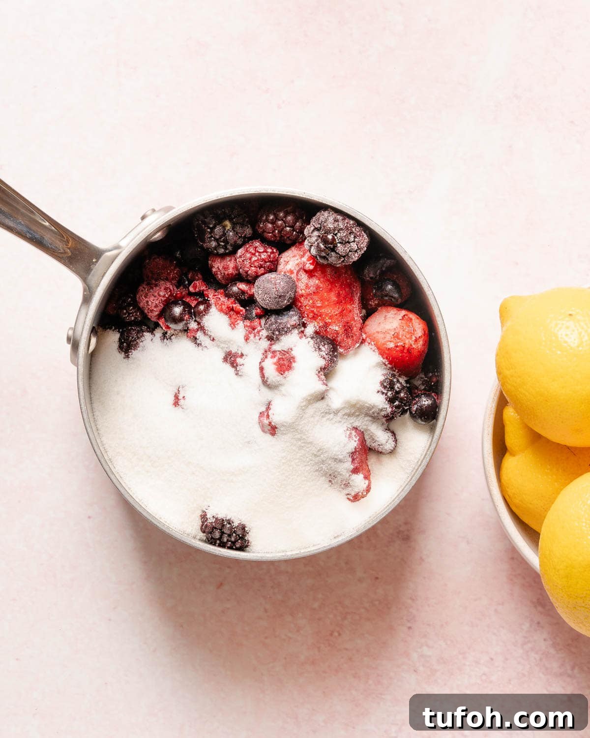 sugar and berries in a pot with lemons on the side.