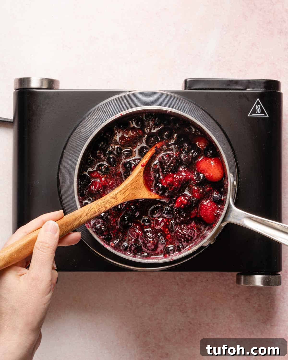 berries and sugar being cooked in small pot on a burner.